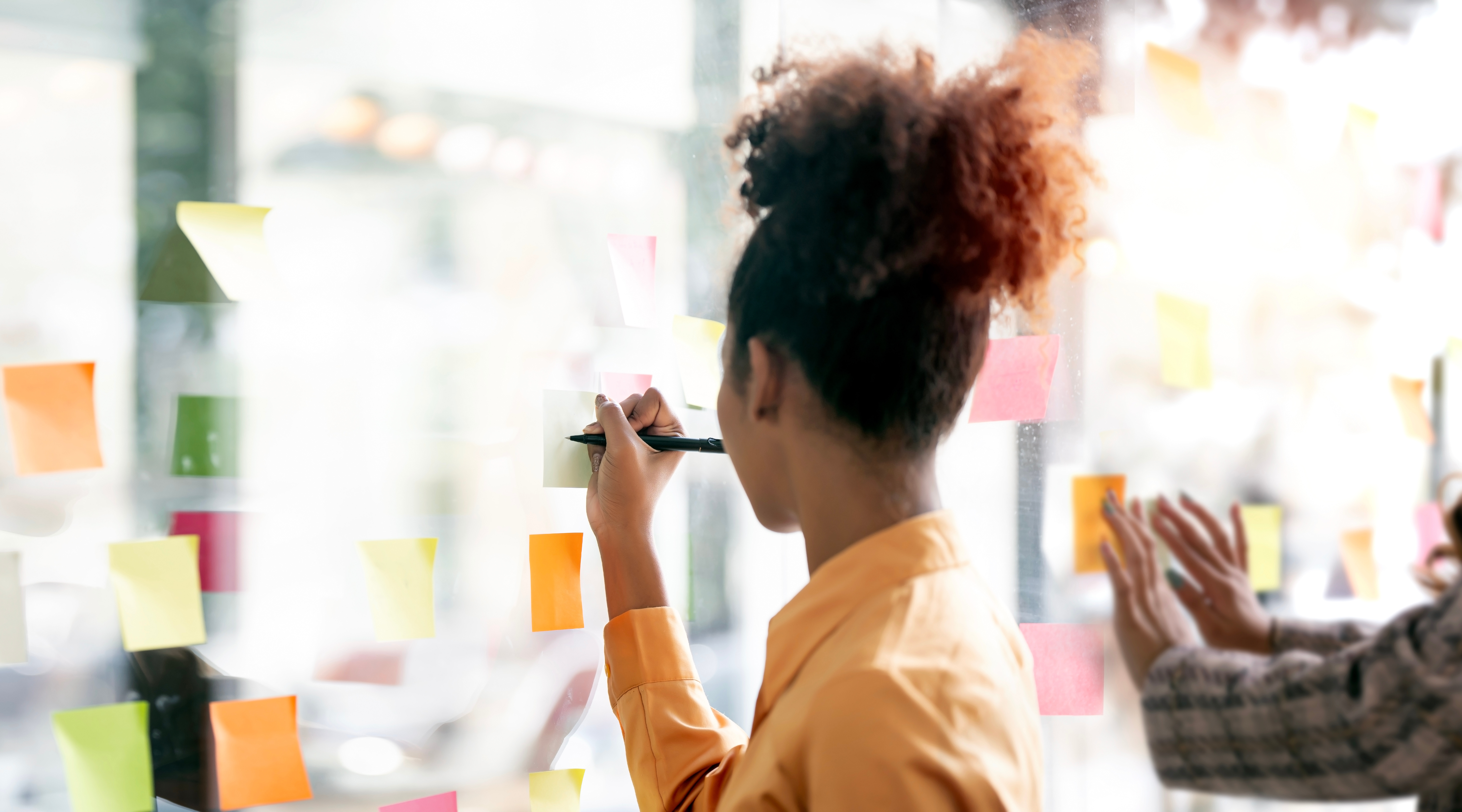 Young businesswoman creative team using post it notes in glass wall to writing strategy business plan to development grow to success.